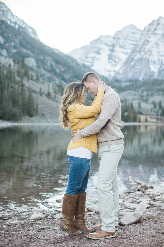 couple in an embrace by the lake with mountains in the background 