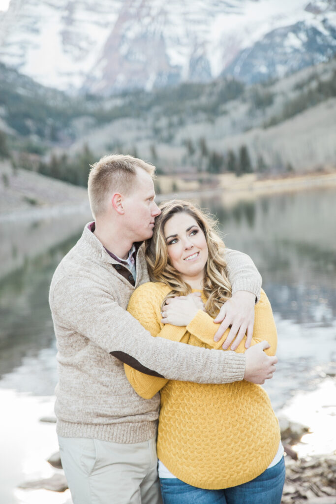 couple laughing and holding hands by the lake with mountains in the background 