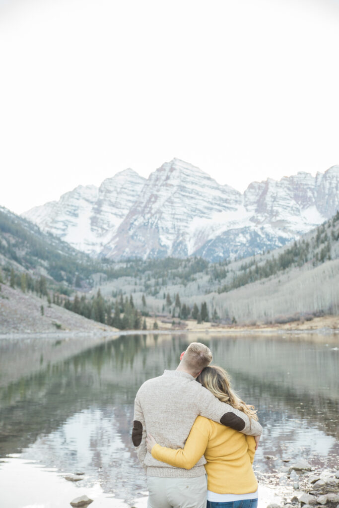 couple from behind looking out toward the mountains in the distance across the lake 