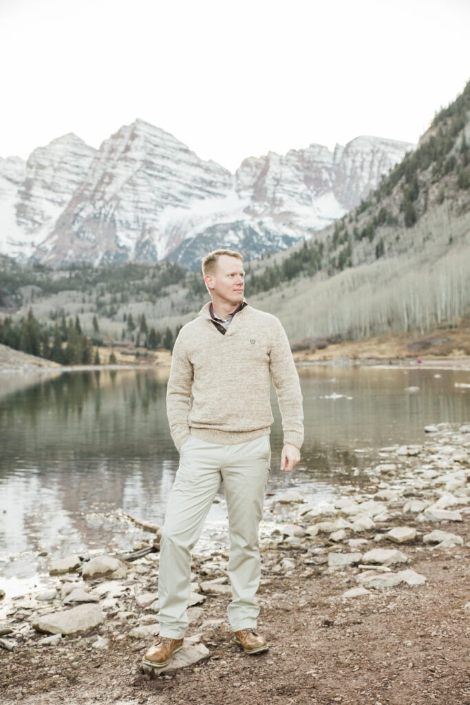 male model wearing a tan sweater and looking into distance with mountains in the background 