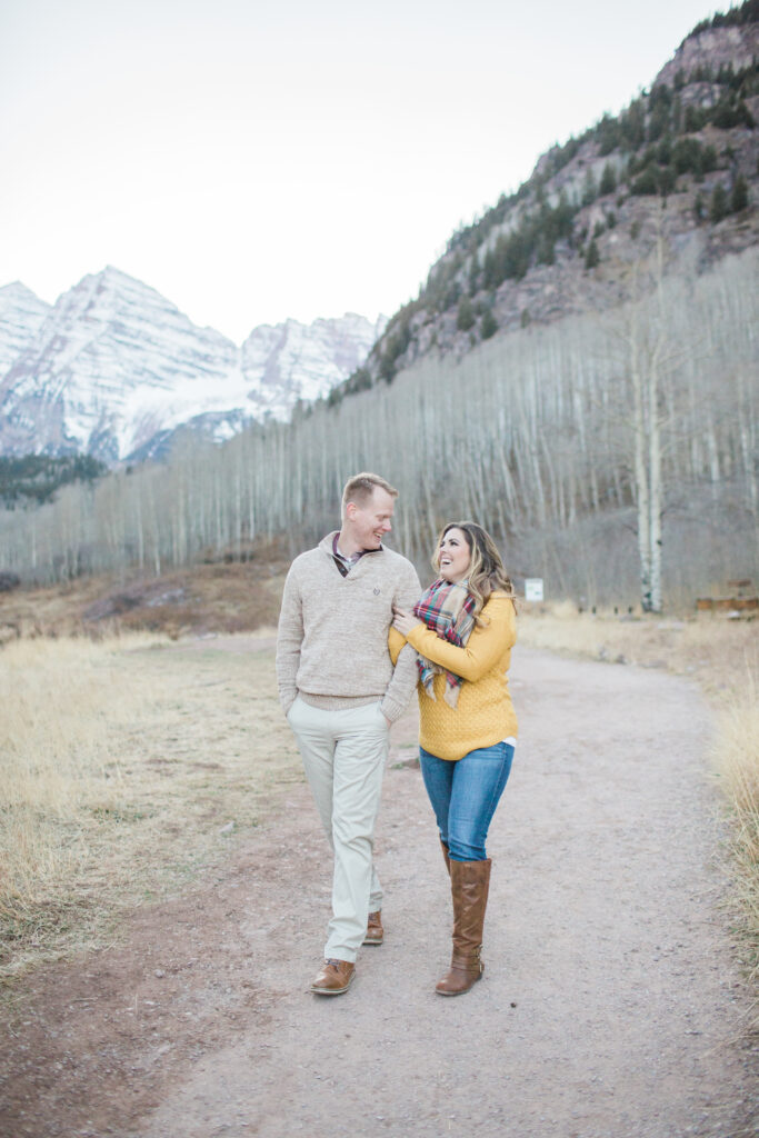 couple holding arms and walking together with mountains in the background 