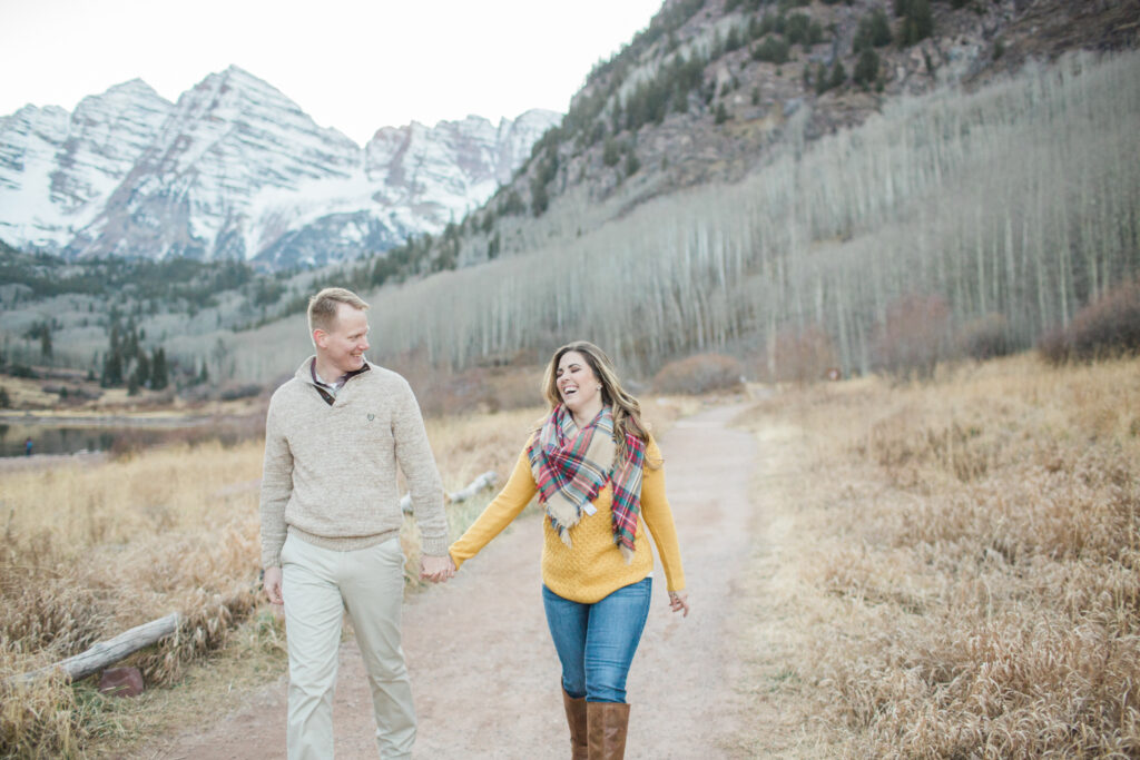 couple holding arms and laughing while walking together with mountains in the background 