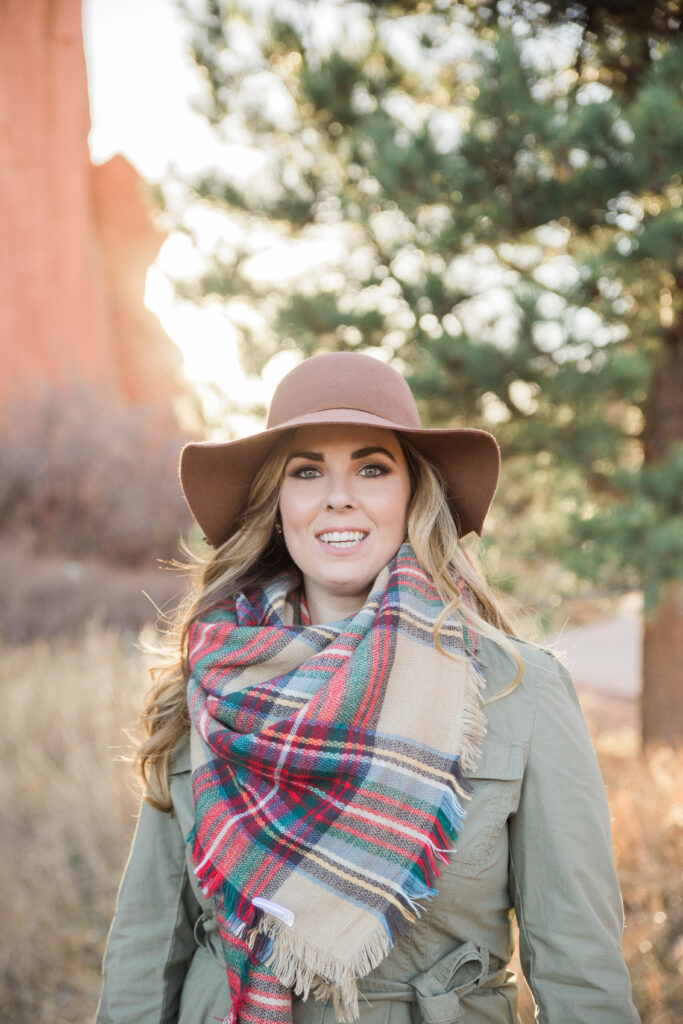 portrait of woman wearing a brown floppy hat, green cargo jacket, and a scarf