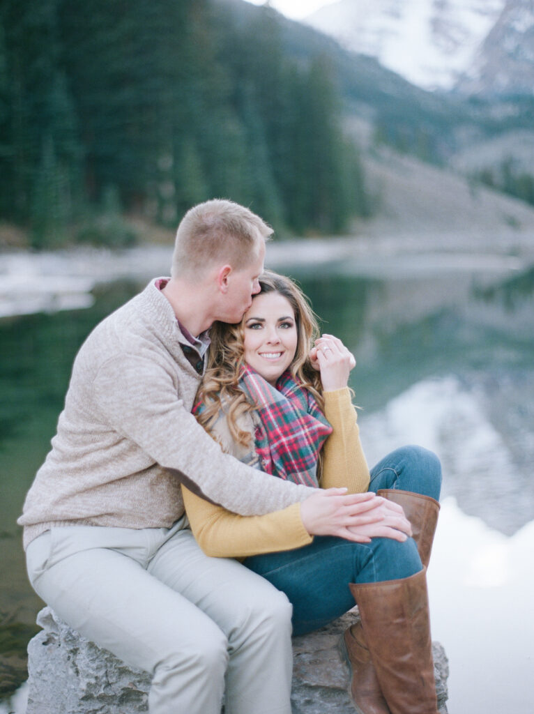 couple snuggling and man kissing forehead of girl on a rock and enjoying nature 