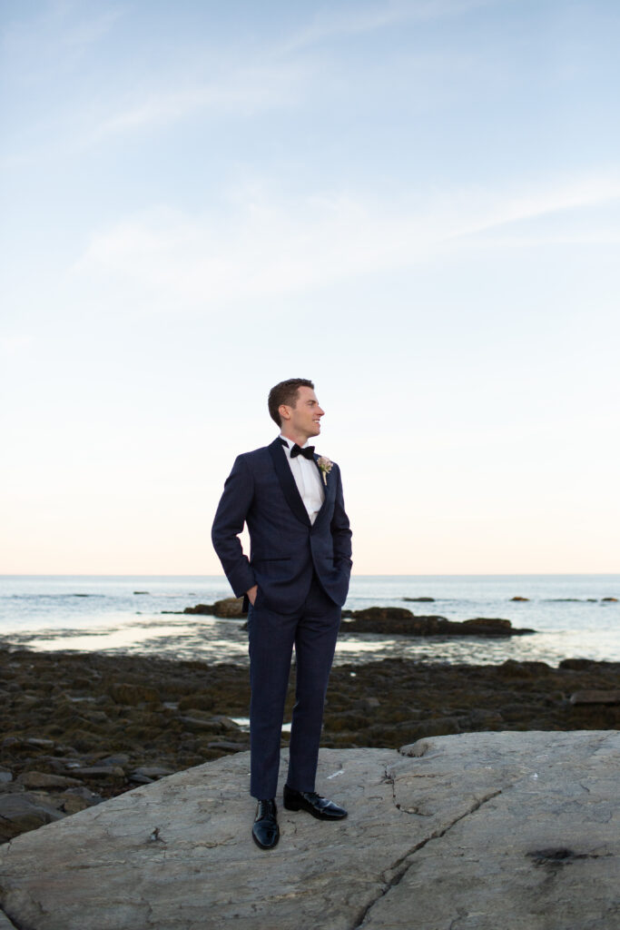 groom looking out at the ocean while he stands on the rocks