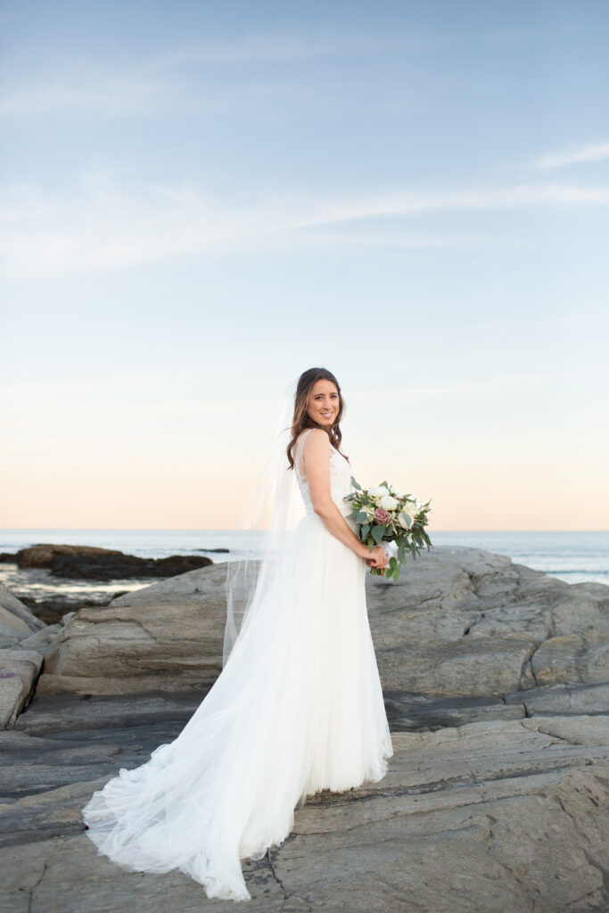 brides veil blowing in the wind while she stands on the rocks