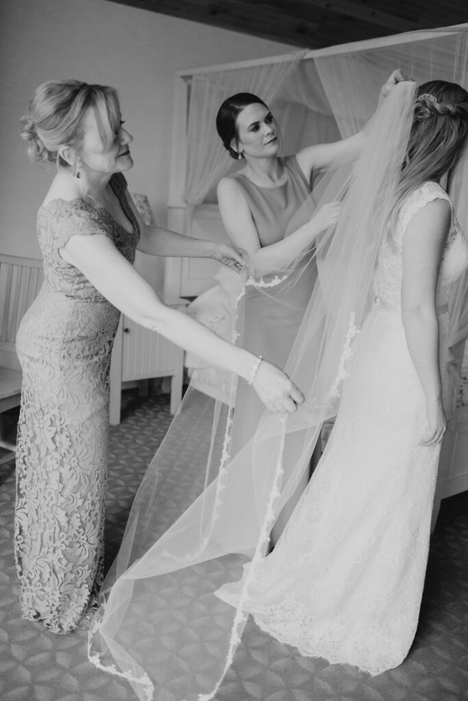 black and white photo of brides mom and sister helping with her veil