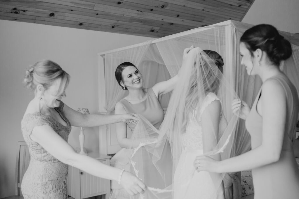 black and white photo of brides friends and family helping with her dress and veil