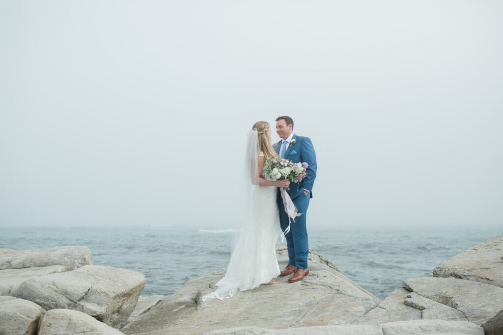 bride and groom on the rocks with the ocean in the background 