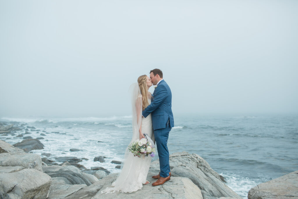 bride and groom kissing on the rocks with the ocean in the background 