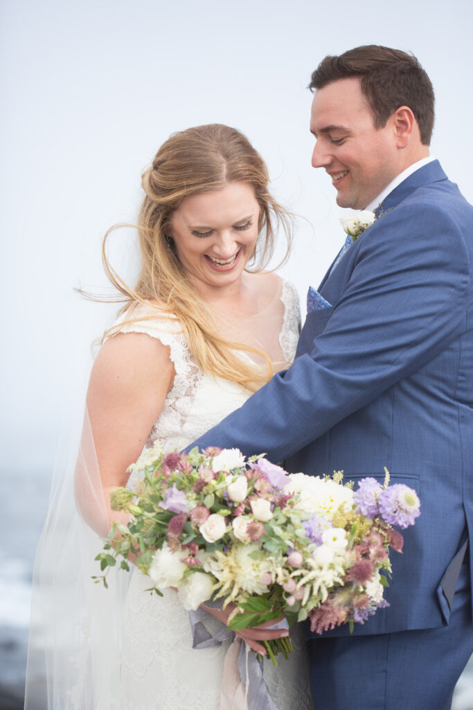 bride and groom laughing on the rocks with the ocean in the background 