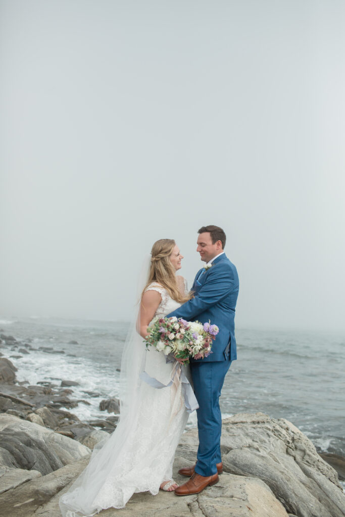 bride and groom on the rocks with the ocean in the background 