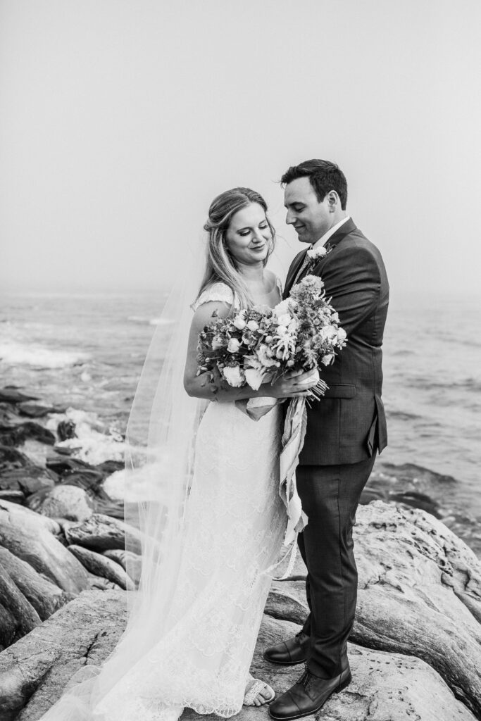 black and white of bride and groom on the rocks with the ocean in the background 