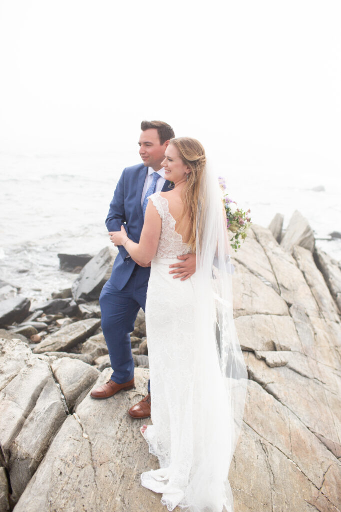 bride and groom on the rocks with the ocean in the background 