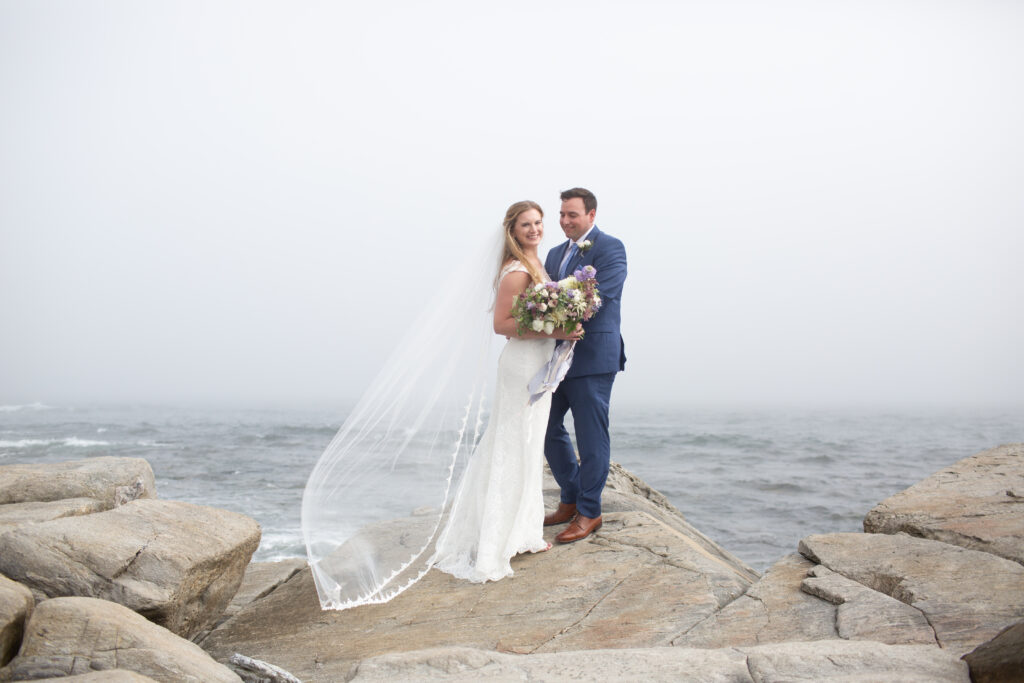 bride and groom on the rocks with the ocean in the background 