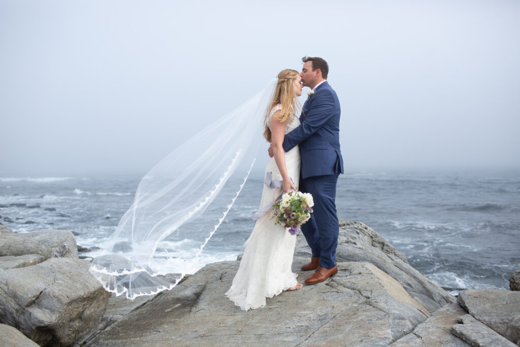 bride with groom kissing her forehead on the rocks with the ocean in the background 