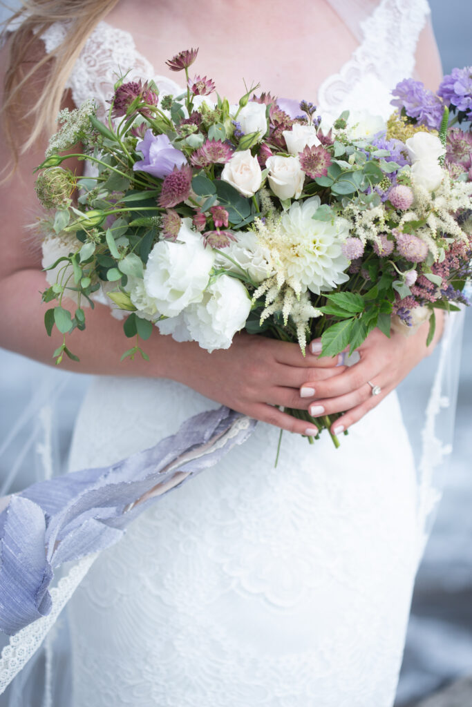 bridal bouquet with a white dahlia, white roses, purple asters, purple clovers, and some eucalyptus tied with periwinkle silk ribbon