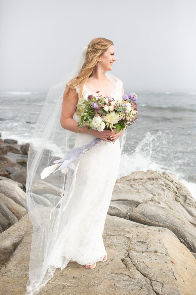 bride looking out at the ocean on the rocks veil blowing in the wind