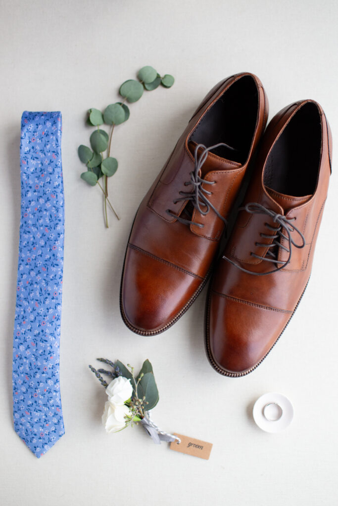 grooms shoes, blue tie, and ring arranged in a flatlay