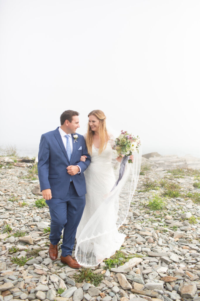 bride and groom walking arm in arm on the rocky beach 