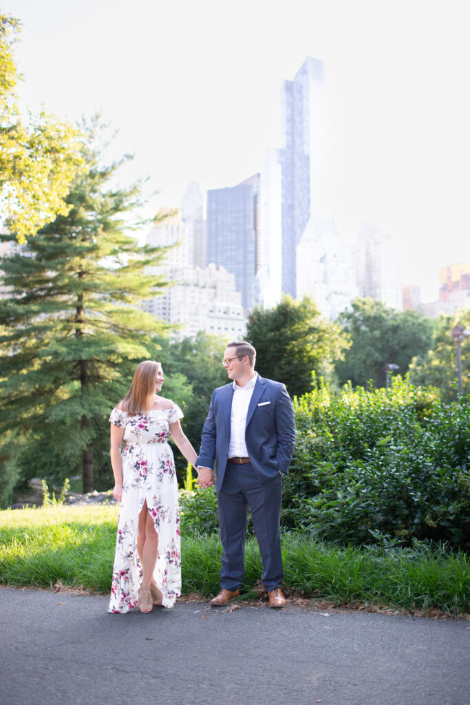 couple holding hands in central park with skyline in the background 