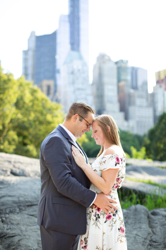 couple leaning forehead to forehead in central park with skyline in the background 