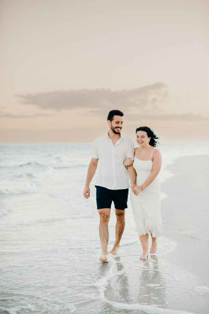 couple walking holding hands with sunset on the beach in the background