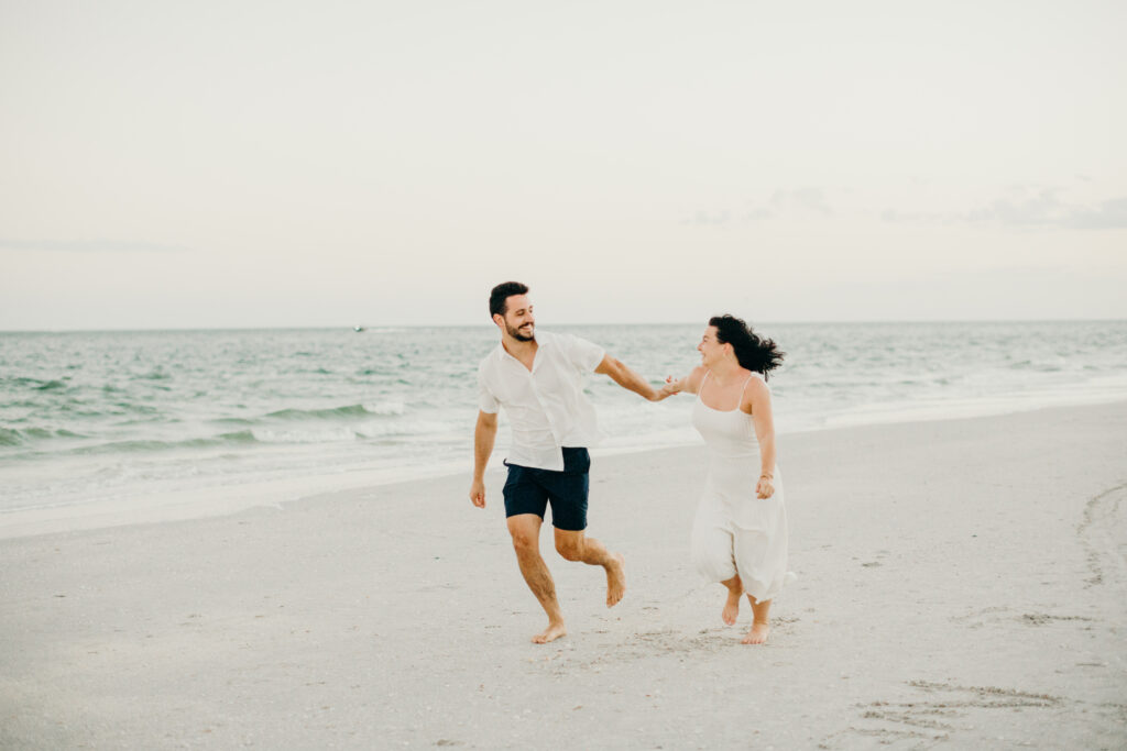 couple running holding hands with sunset on the beach in the background