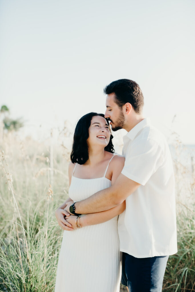 couple laughing with each other with dune grass in the background 