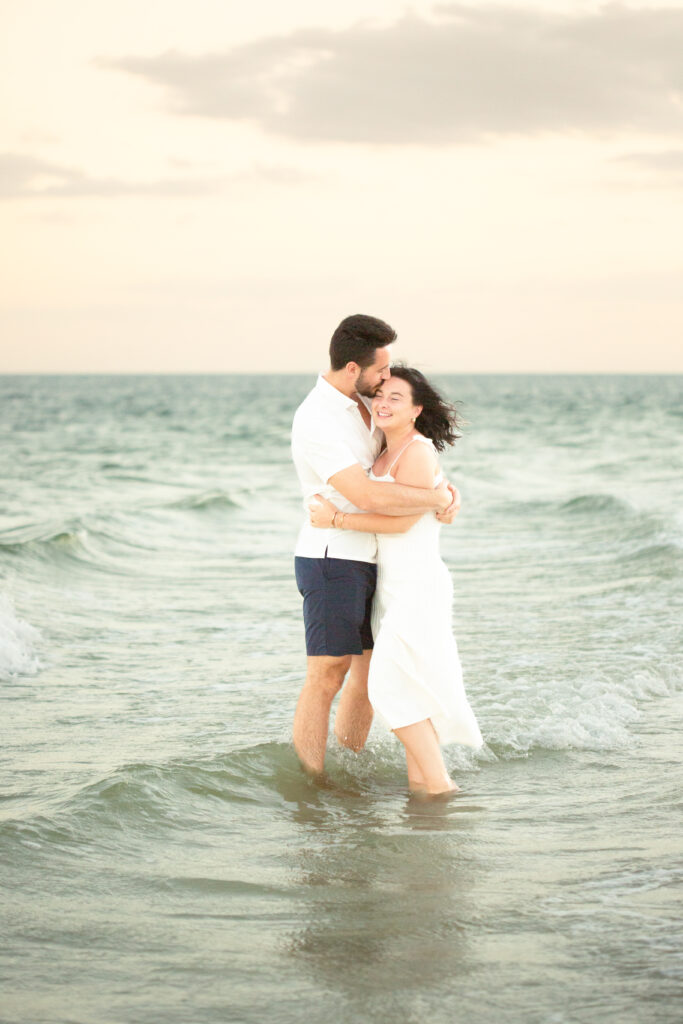 couple standing in the waves on the beach at sunset 