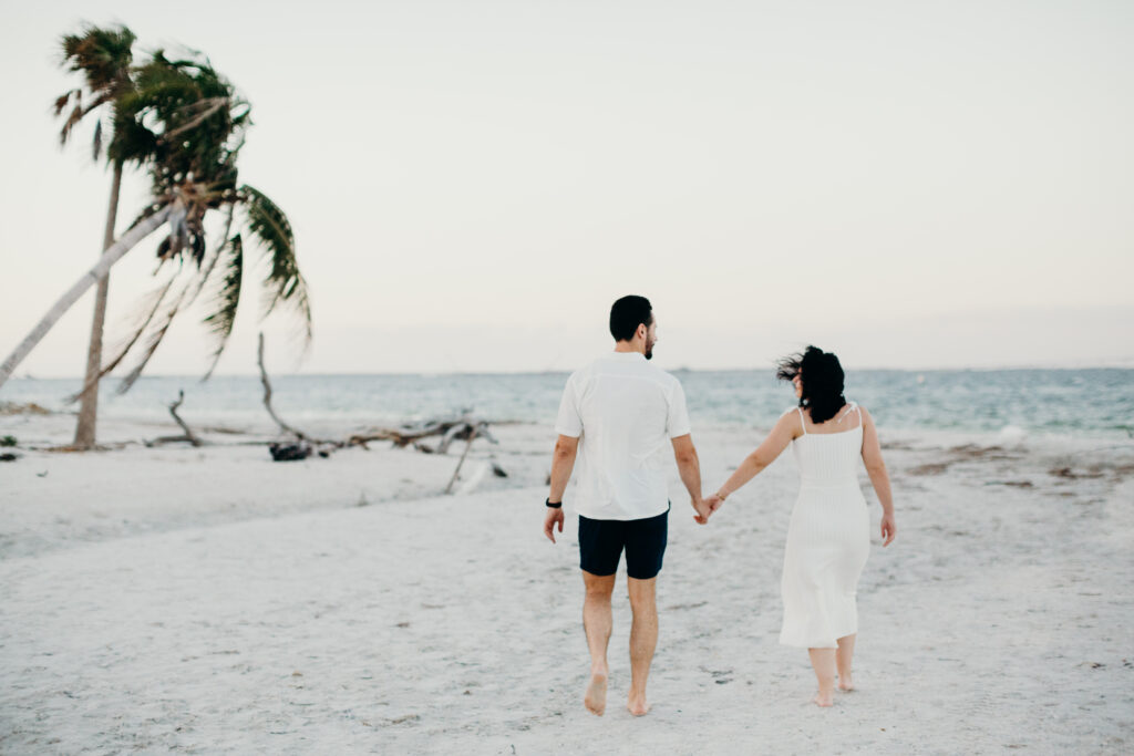 couple holding hands on the beach with the wind blowing her hair