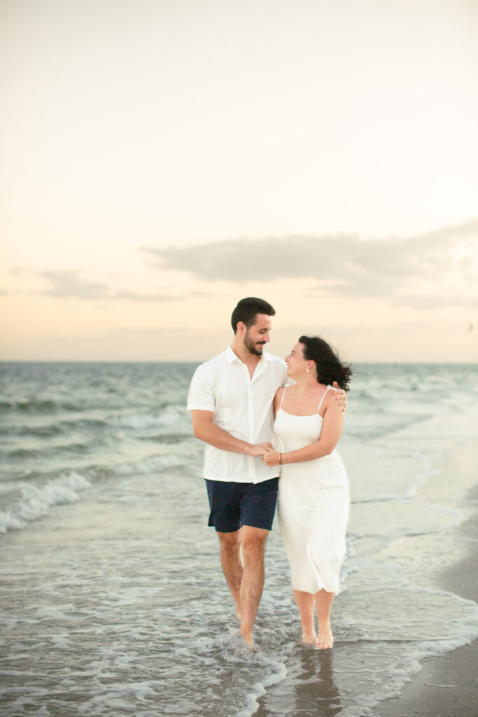 couple walking holding hands with sunset on the beach in the background