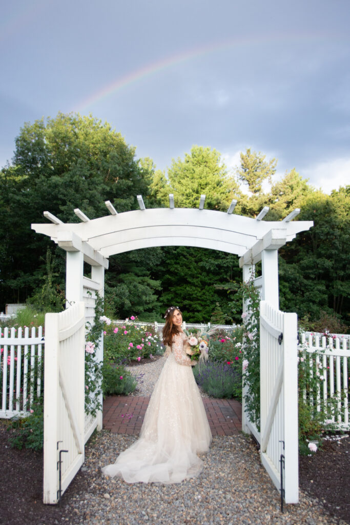 bride playing with dress in rose garden with rainbow in the background 