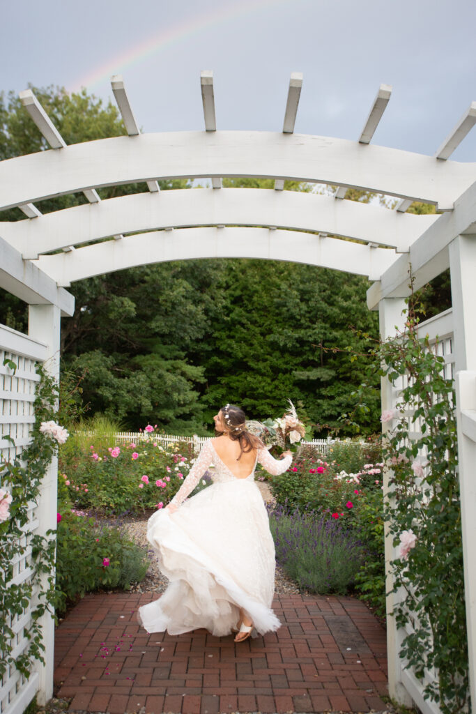 bride playing with dress in rose garden with rainbow in the background 