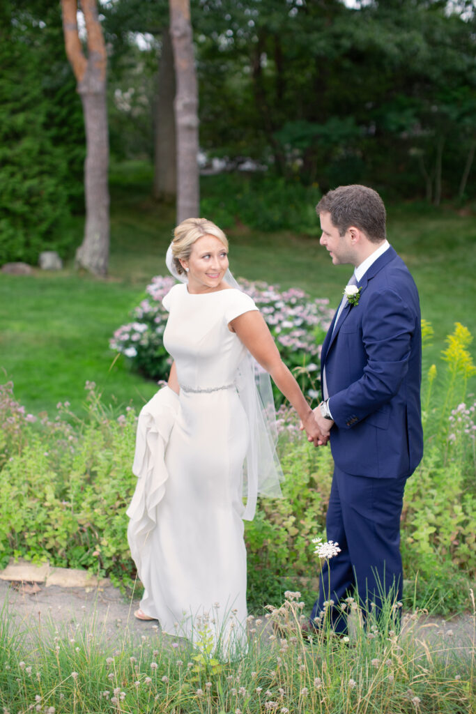 groom in navy and bride standing in the gardens 