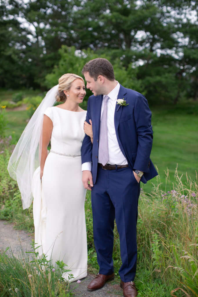 groom in navy suit with bride standing in the gardens 