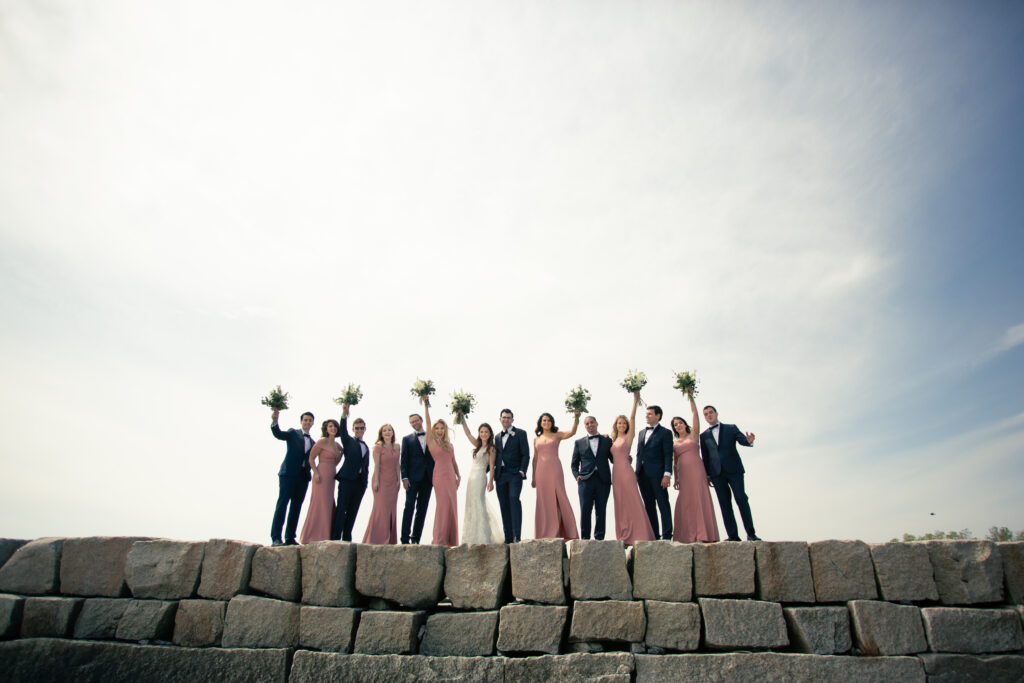 wedding party on rocky jetty with flowers in the air cheering 