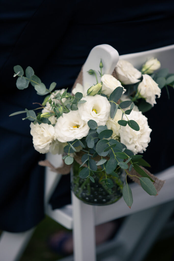 white flowers in vase hanging off white chairs for the ceremony 