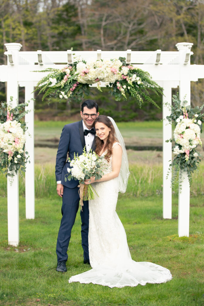 bride and groom in front of white wooden alter with flowers 