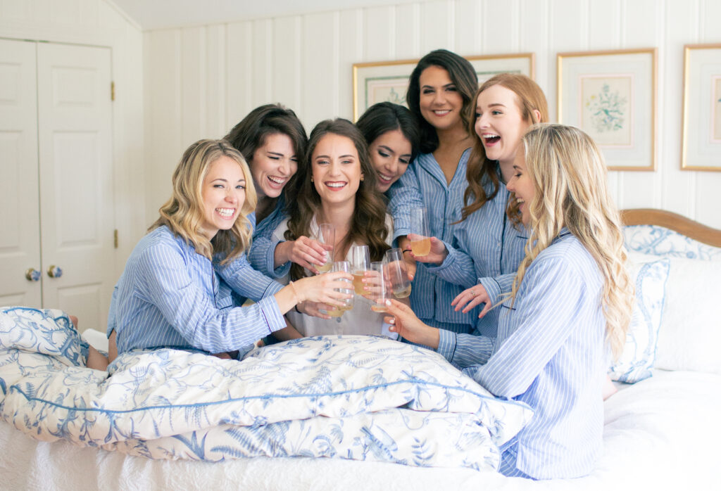 bridesmaids laughing having mimosas on bed wearing matching blue pajamas 