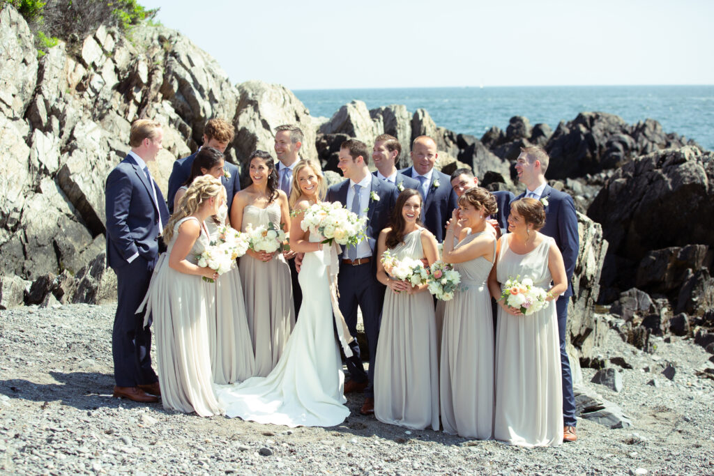 wedding party laughing and standing on a rocky beach