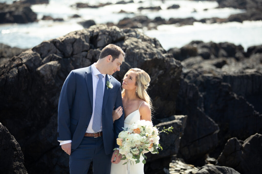 bride and groom looking at each other on a rocky beach