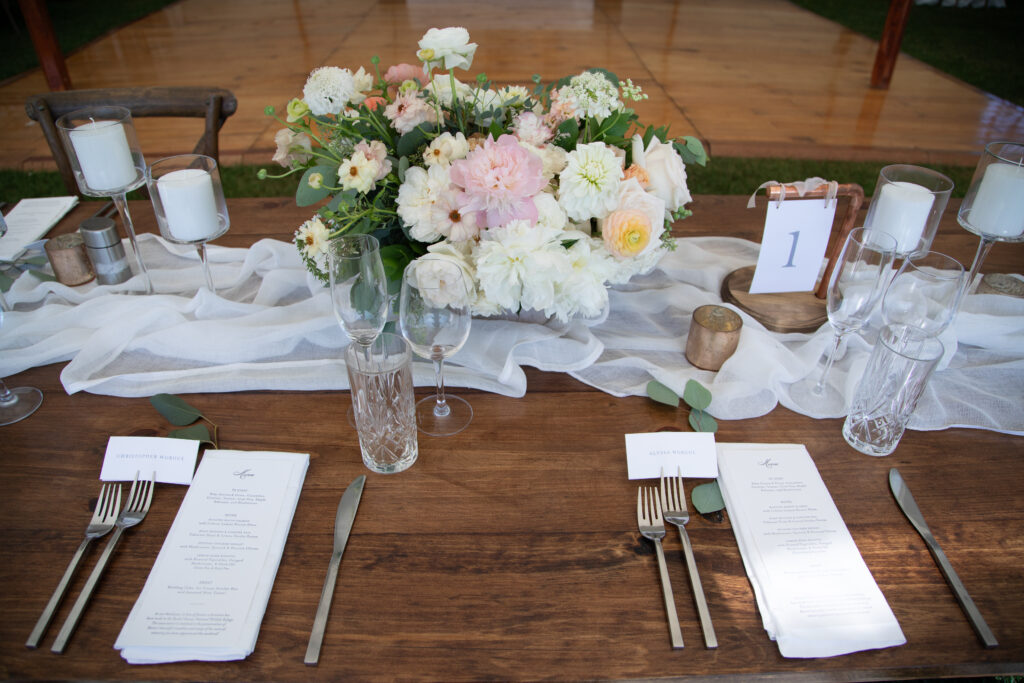 long wooden reception tables with runner and floral centerpieces made from peonies, dahlias, and ranunculus flowers