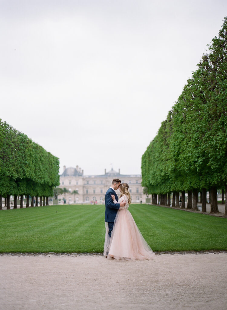 bride and groom in front of a lush green space at the jardin de luxembourg 