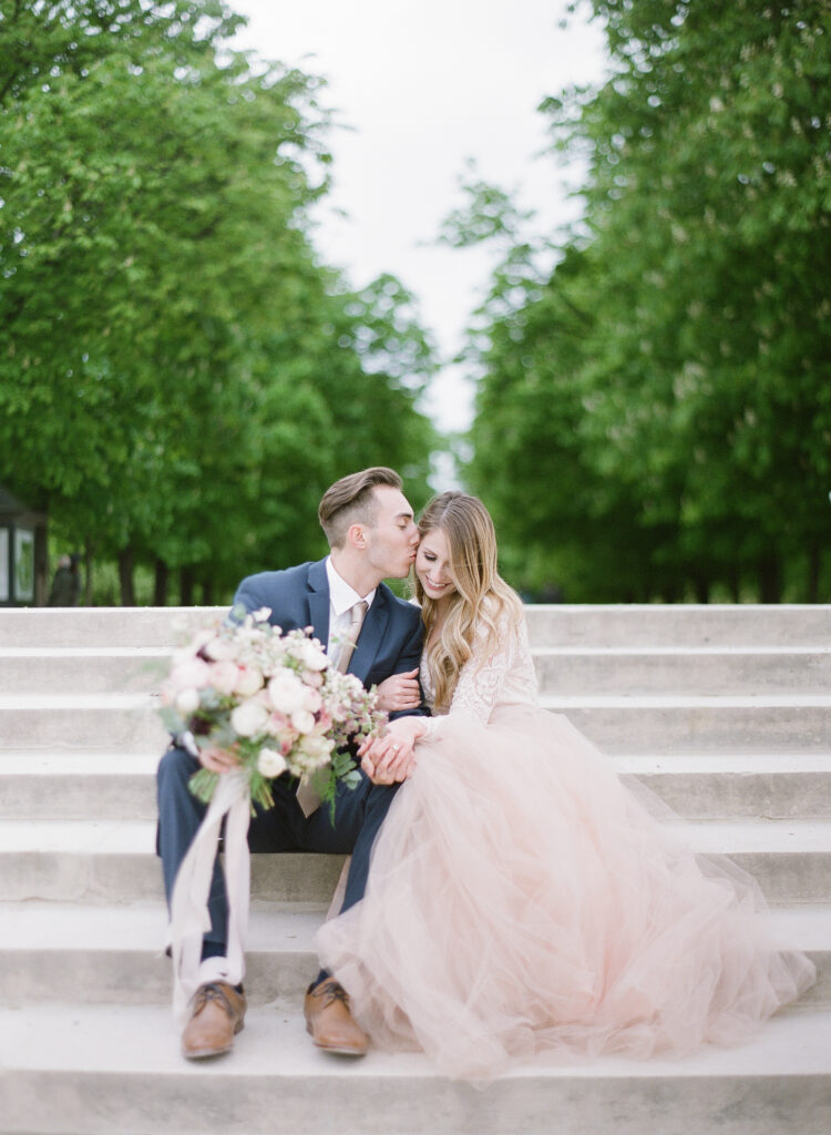 groom kissing brides cheek while sitting next to each other on the steps 