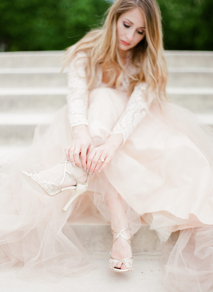 bride sitting down and fastening her shoes 