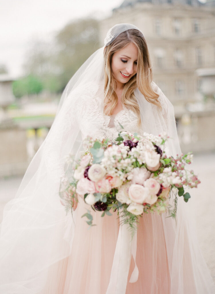 bride wearing blush colored lace gown holding a bouquet full of white and blush colored flowers