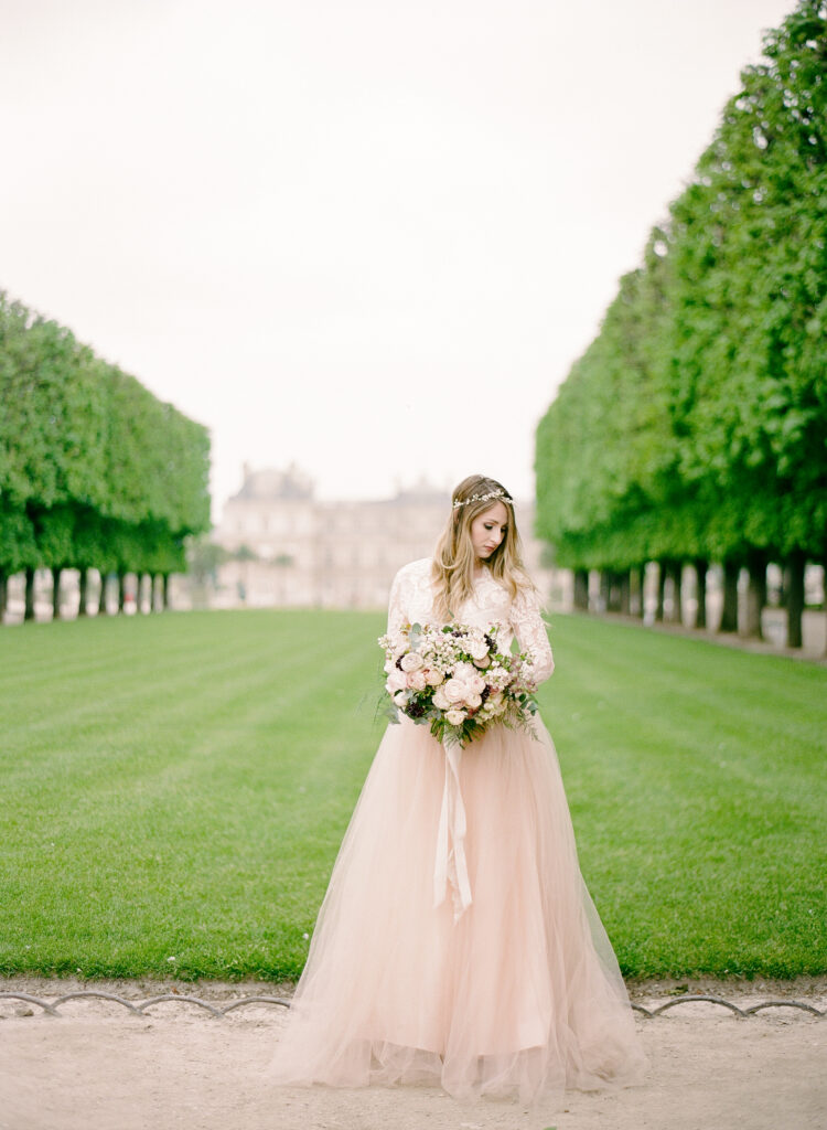 bride wearing blush gown against a large lawn at the jardin de luxembourg