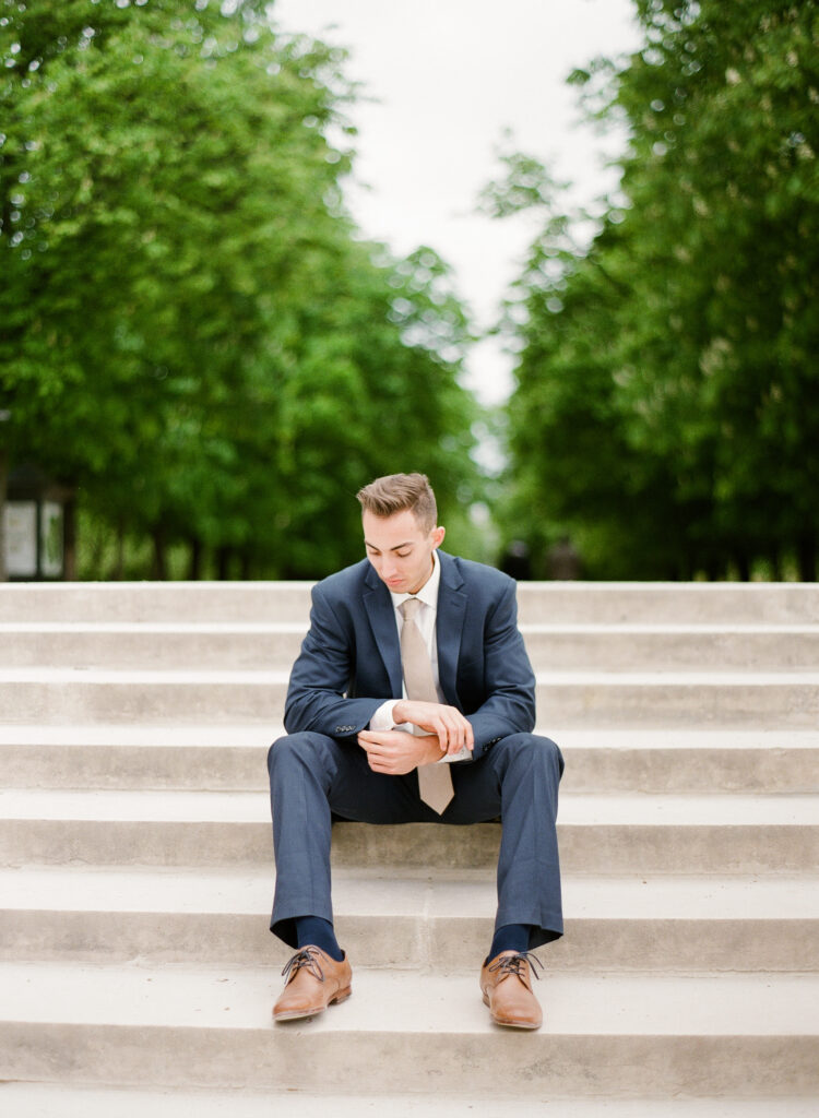 groom sitting on steps in jardin de luxembourg wearing blue suit