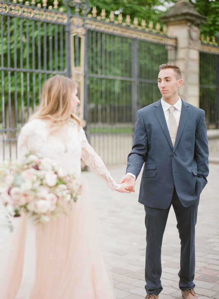 bride and groom walking in front of gilded iron gate in Paris 